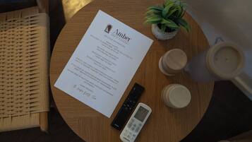 Een ronde houten tafel met een afstandsbediening, een Samsung telefoon, een kleine potplant en een welkomstkaart voor hotel Amber.