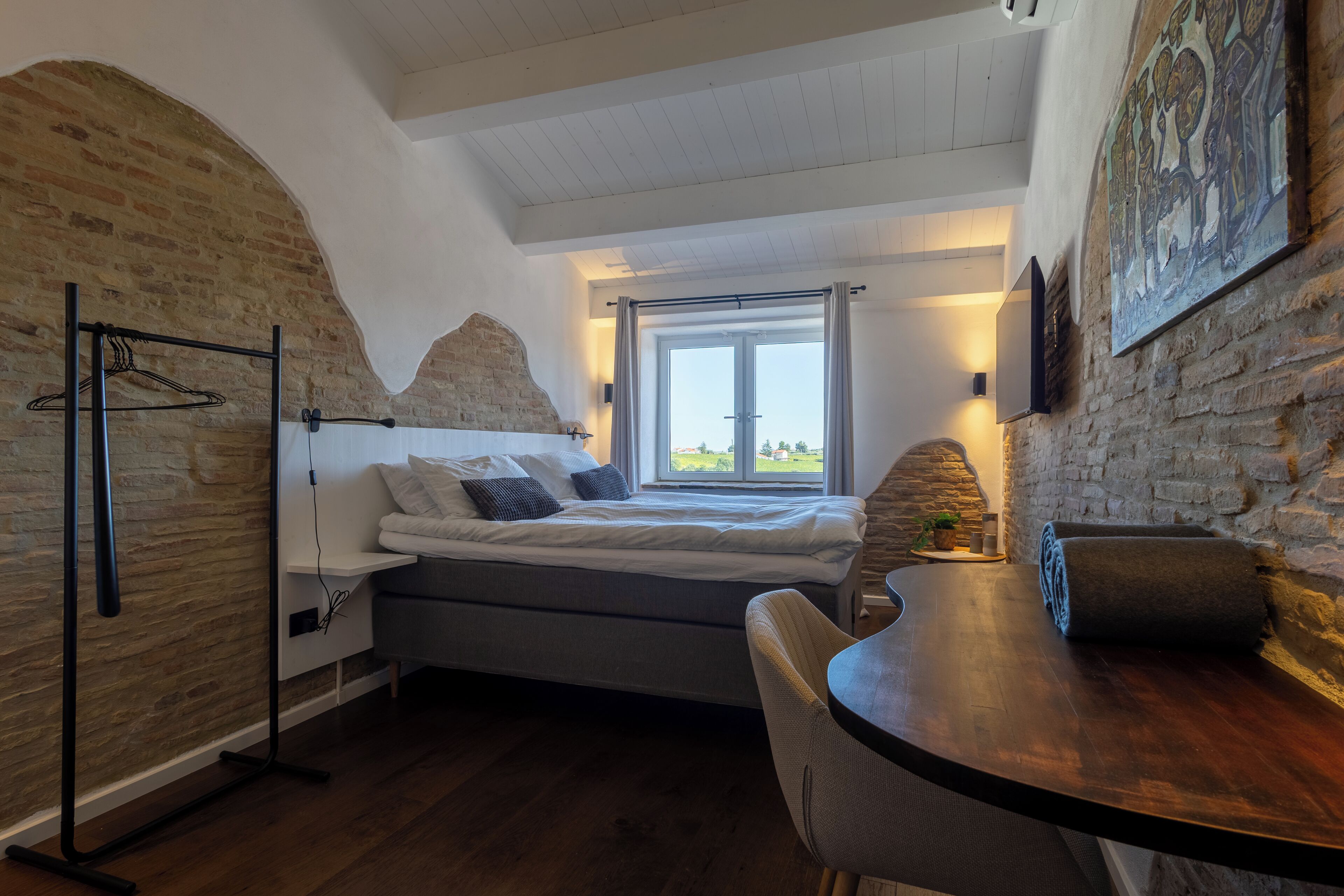 A bedroom with a bed, a desk, and a window.