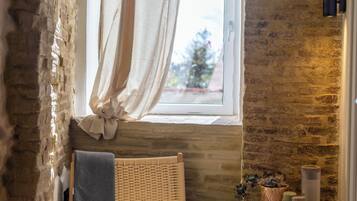 A cozy room with a stone wall, a wicker chair, a small table with a basket, and a window with curtains.