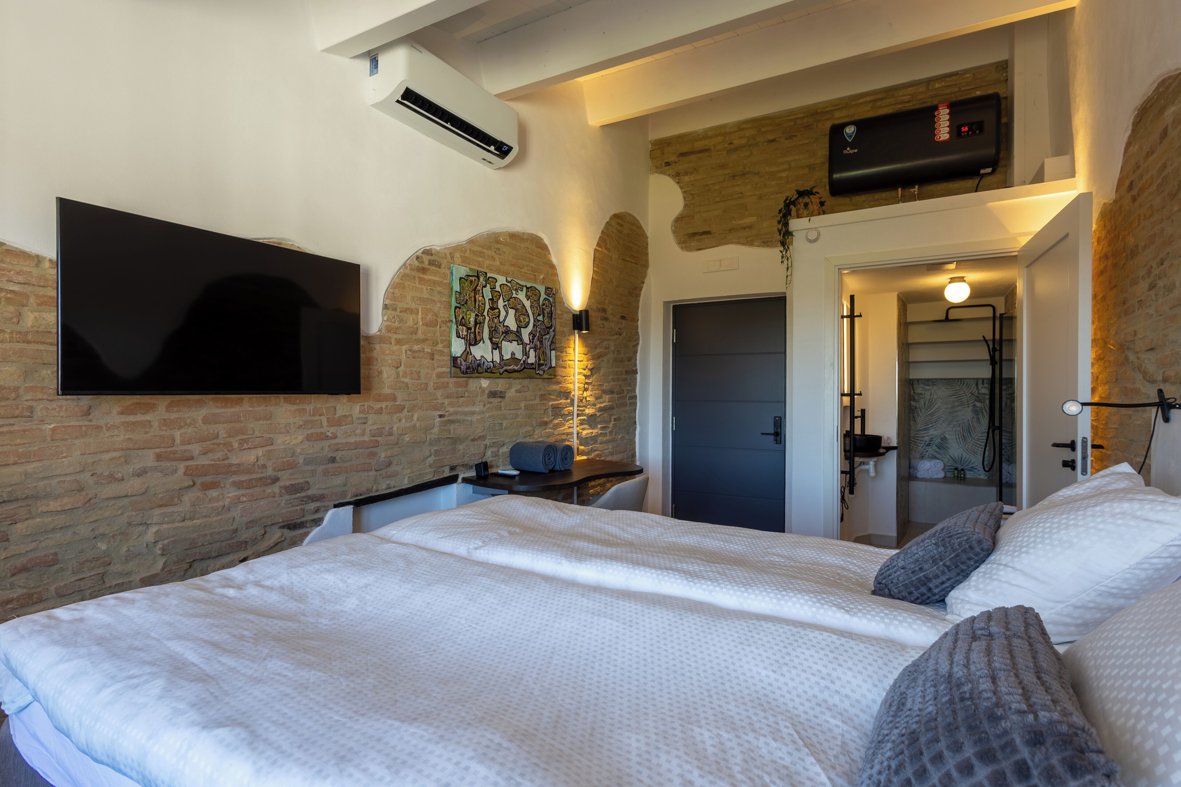 Een slaapkamer met een groot bed, een flatscreen televisie aan de muur, een verwarming en een deur naar een badkamer.