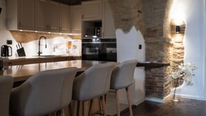 A kitchen with white cabinets, a wooden countertop, and a stone wall. There are two bar stools and a vase with flowers on the counter.