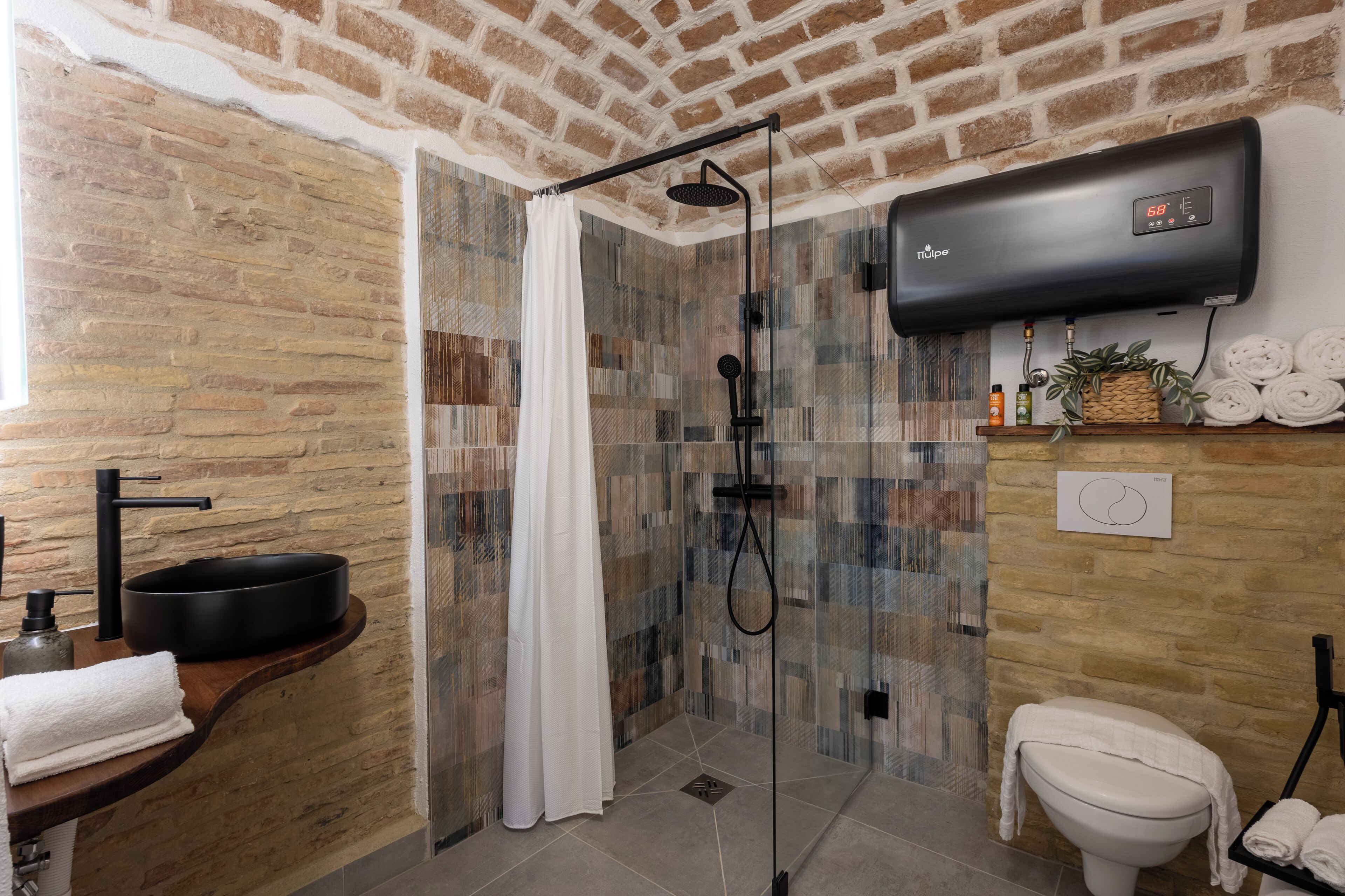 A bathroom with a shower, a toilet, a sink with a black basin, and a towel rack.