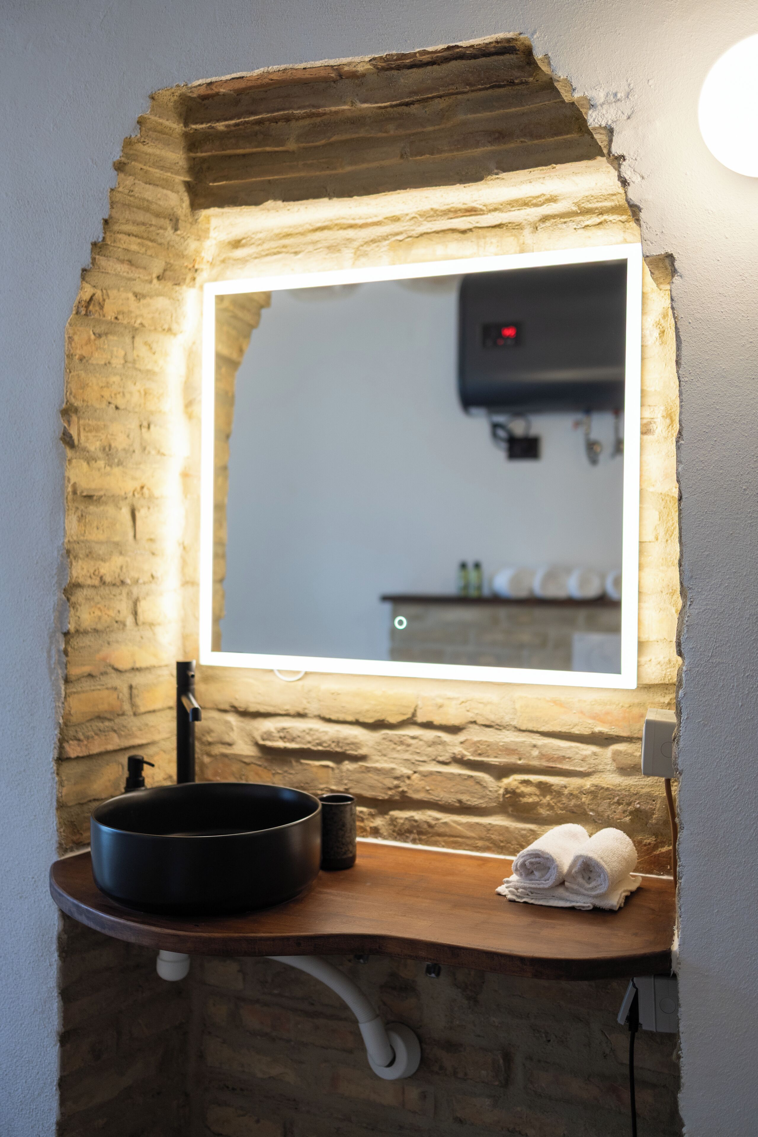 Un bagno con arco in pietra, uno specchio con luce, un lavandino e un portascopevoli.