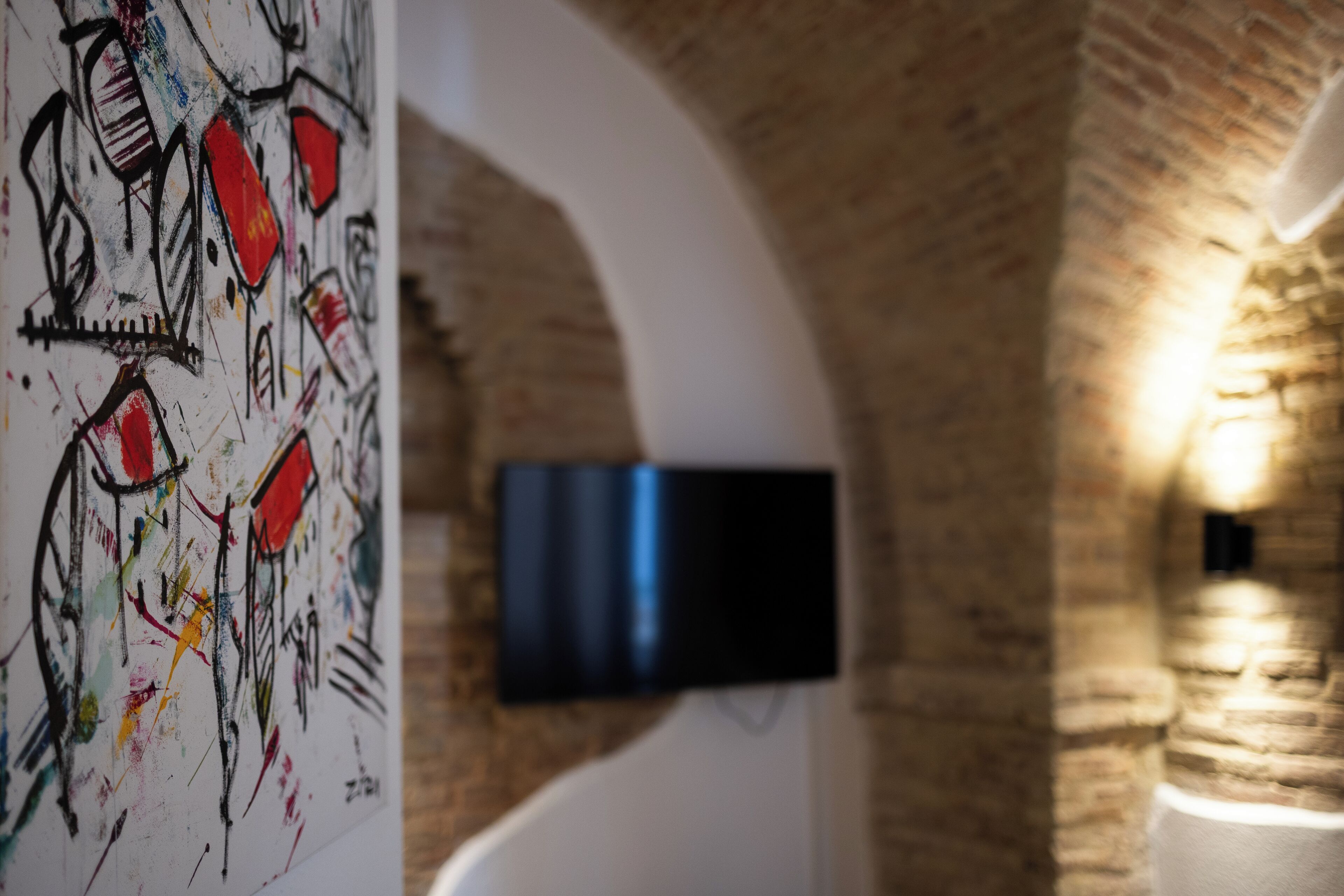 A room with a brick wall, a flat-screen TV mounted on the wall, and a colorful abstract painting on the left.