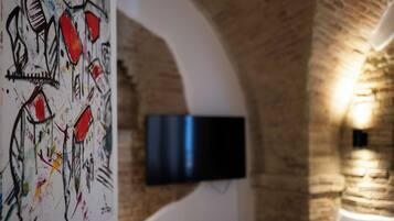 A room with a brick wall, a flat-screen TV mounted on the wall, and a colorful abstract painting on the left.