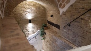 A stone-walled corridor with a wooden staircase and a hanging plant.