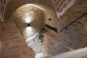 Un pasillo de paredes de piedra con una escalera de madera y una planta colgante.