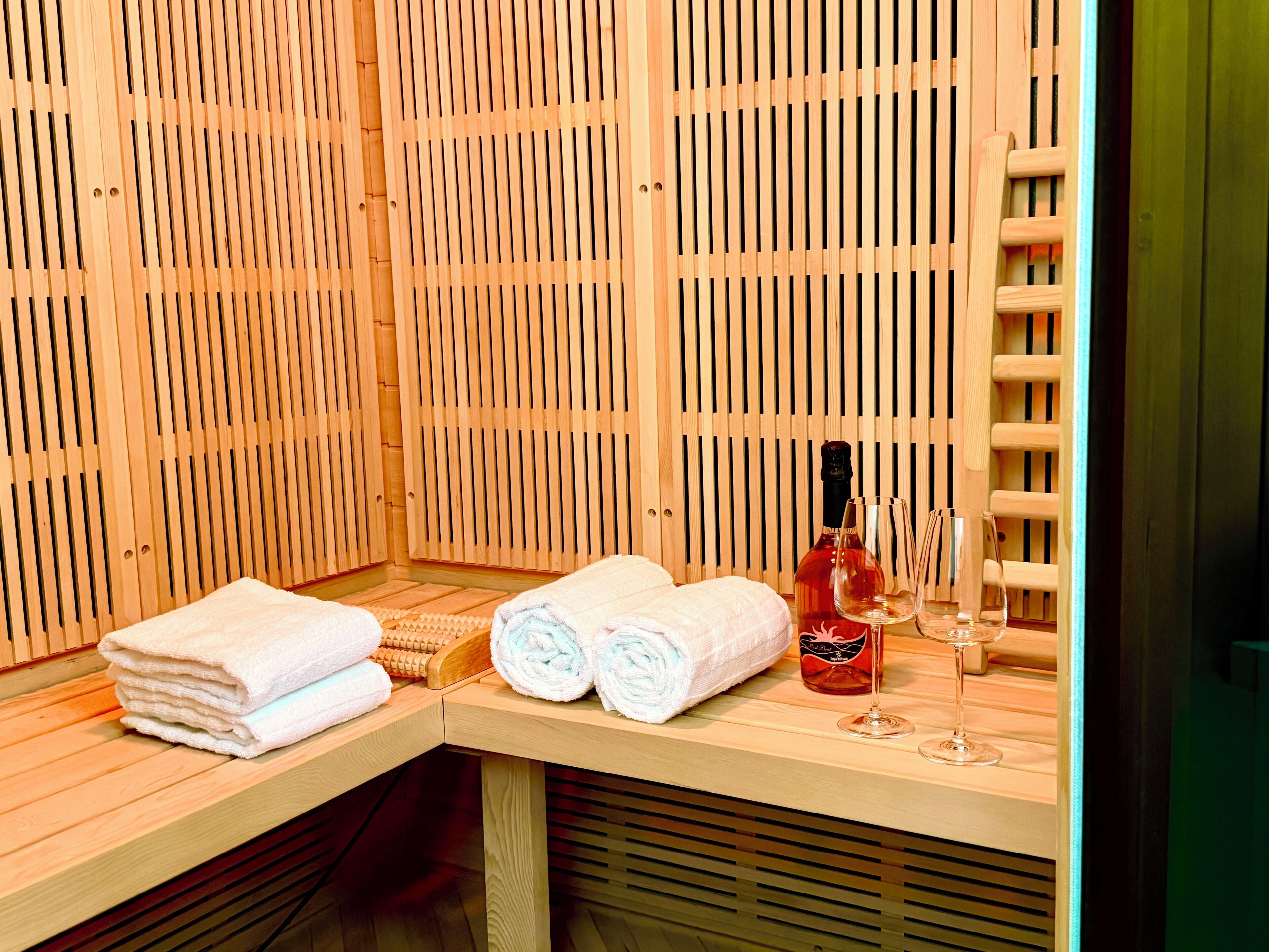 Una sala de sauna con listones de madera, un banco, toallas y una botella de vino.