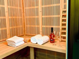 Una sala de sauna con listones de madera, un banco, toallas y una botella de vino.