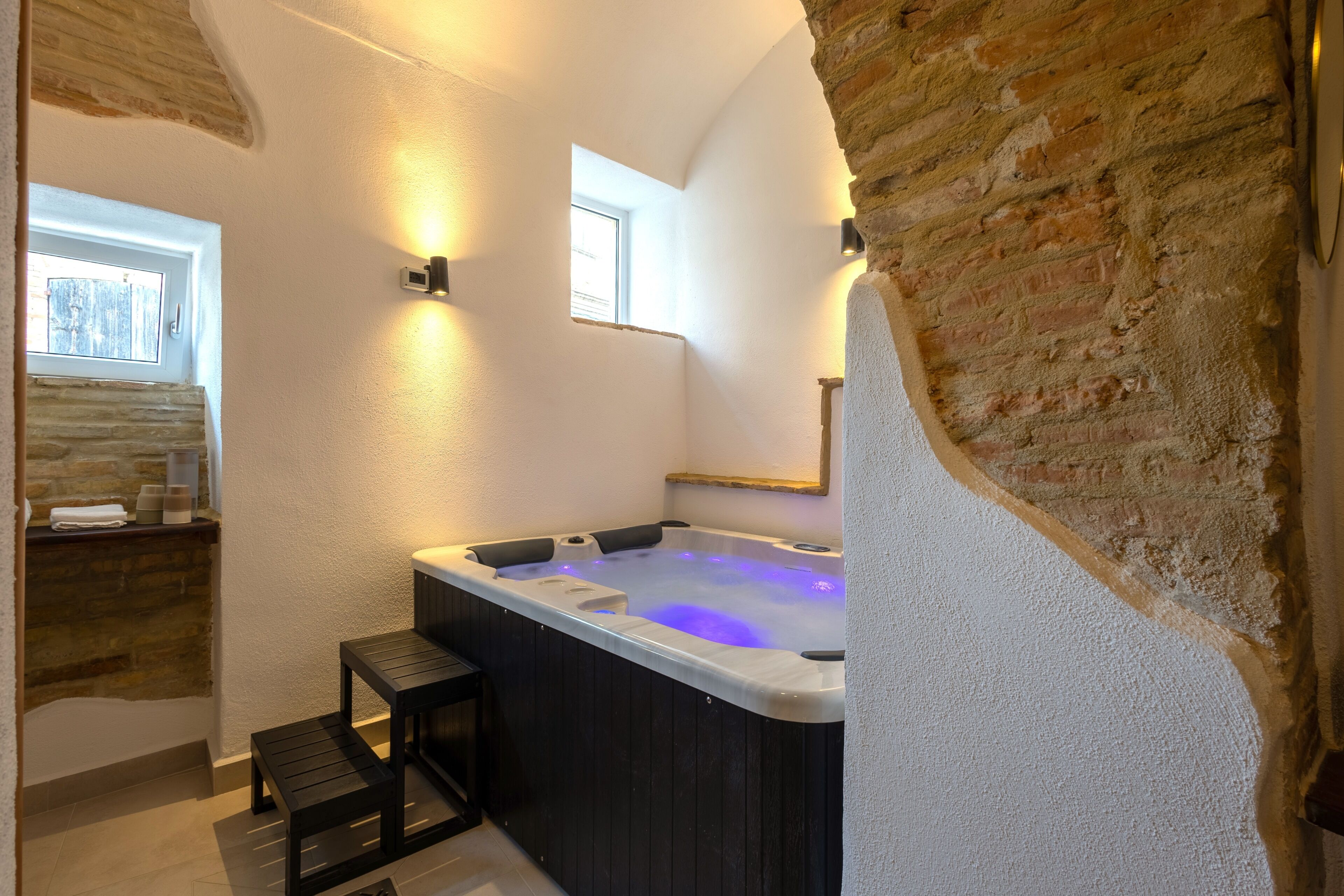 A modern bathroom with a stone wall, a bathtub, and a small wooden stool.