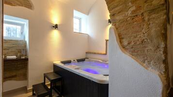 A modern bathroom with a stone wall, a bathtub, and a small wooden stool.