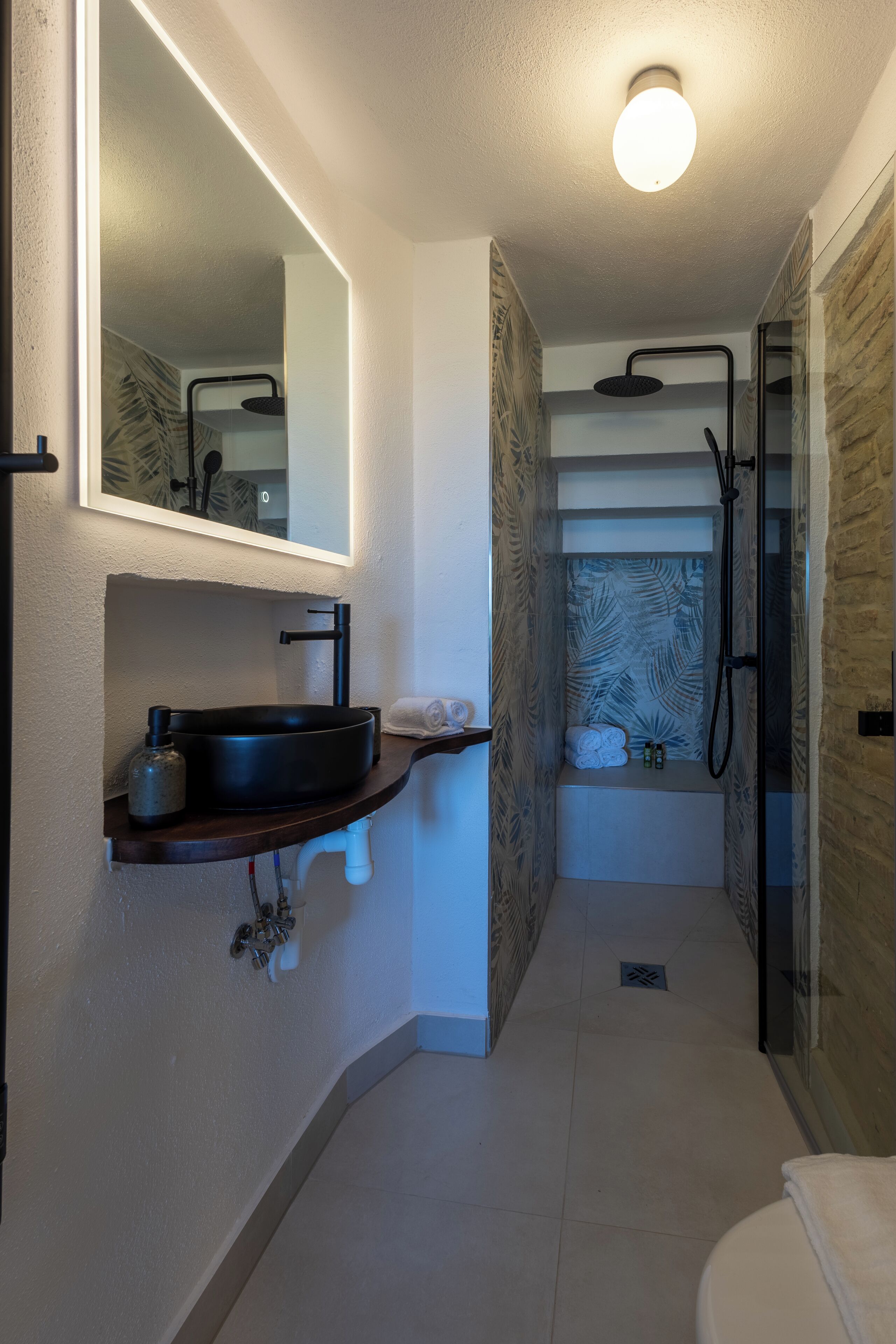 A modern bathroom with a black sink, a mirror, a shower, and a towel rack.