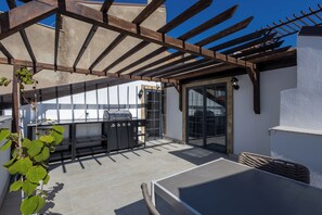 An outdoor patio with a grill, a dining table, and a pergola structure.