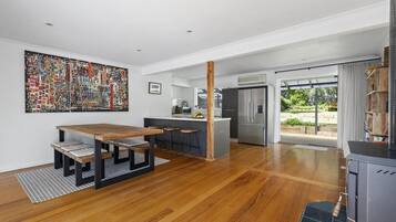 Una cocina moderna con una isla central, un comedor con mesa y bancos de madera, y un ventanal que ofrece vistas al exterior.