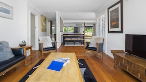 A spacious living room with a wooden coffee table, two sofas, a TV, and a kitchen in the background. - Cooinda, Red Hill South - Serene Red Hill South Retreat surrounded by gardens. (Red Hill South)