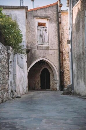 A narrow alleyway with a stone building featuring an arched entrance and a window with wooden shutters.