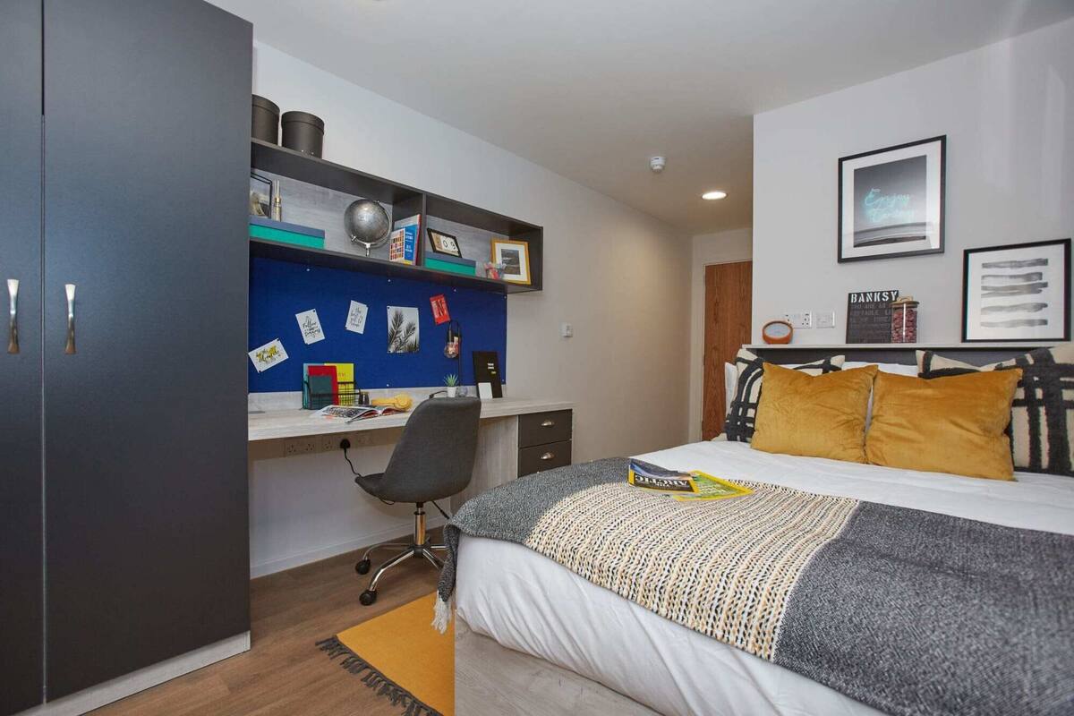 A bedroom with a bed, a desk, and a wardrobe.