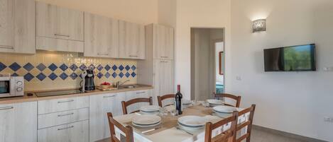 Una cocina moderna con armarios de madera clara, microondas y cafetera. Hay una mesa de comedor con platos, vasos y cubiertos.