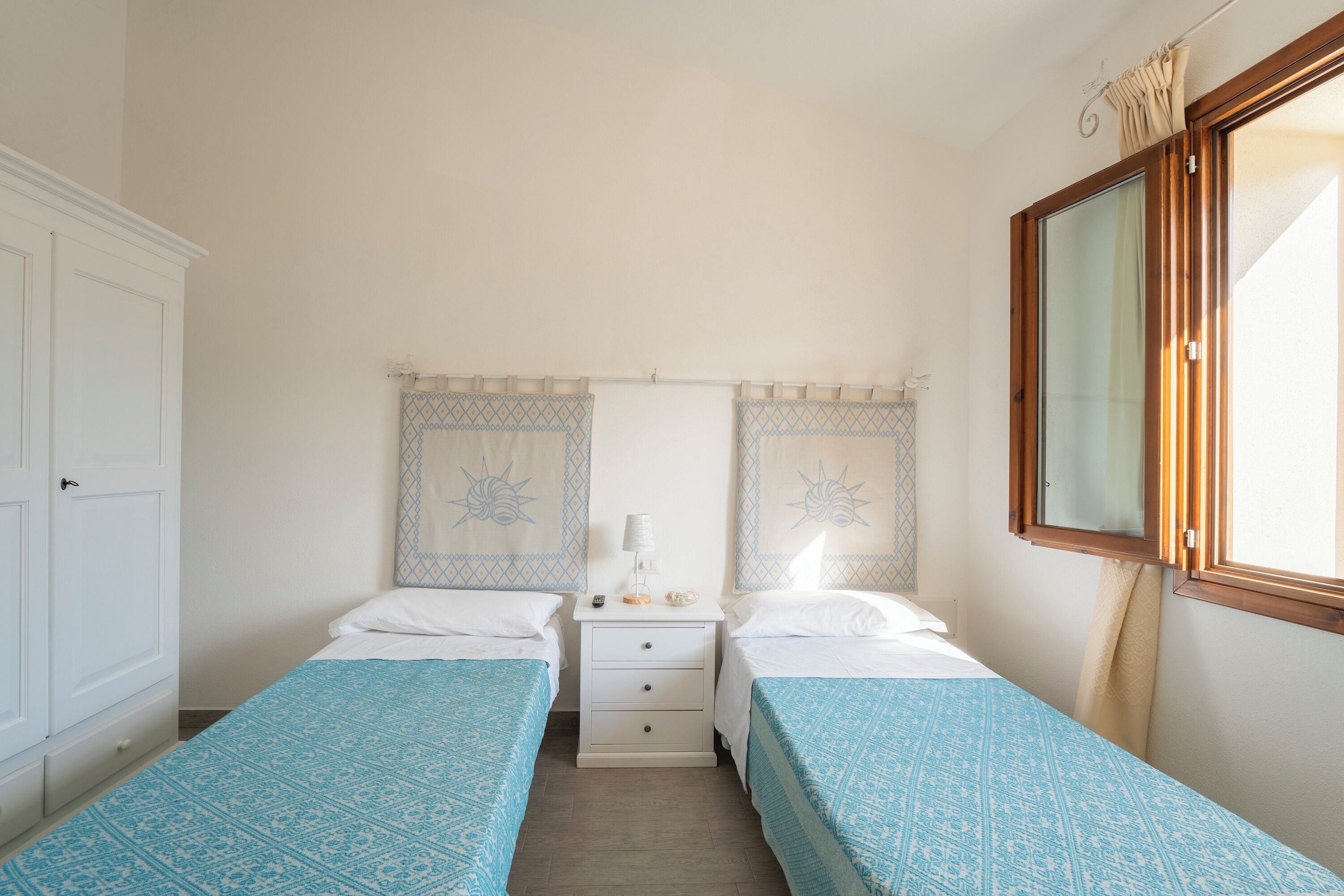 A bedroom with two beds, a nightstand, and a wardrobe.