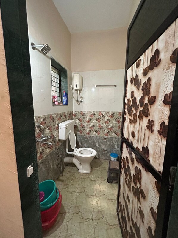 Une petite salle de bain comprenant des toilettes, une douche et un sèche-mains. Il y a une fenêtre donnant sur l’extérieur, ainsi qu’un mur décoratif orné d’un motif floral.