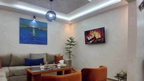 Una sala moderna con un sofá, dos sillones, una mesita de centro y un cuadro de un atardecer sobre el agua.