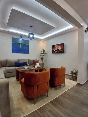 A modern living room with a sofa, two armchairs, a coffee table, and a painting of a sunset over water. - Moga Haven, a haven of peace and charm in Essaouira with a large terrace (Essaouira)