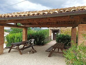 An outdoor patio with two wooden picnic tables, surrounded by gravel, under a wooden pergola. - Agriturismo Alla Vecchia Quercia - Montaiate small apartment for 2 persons (Marche)