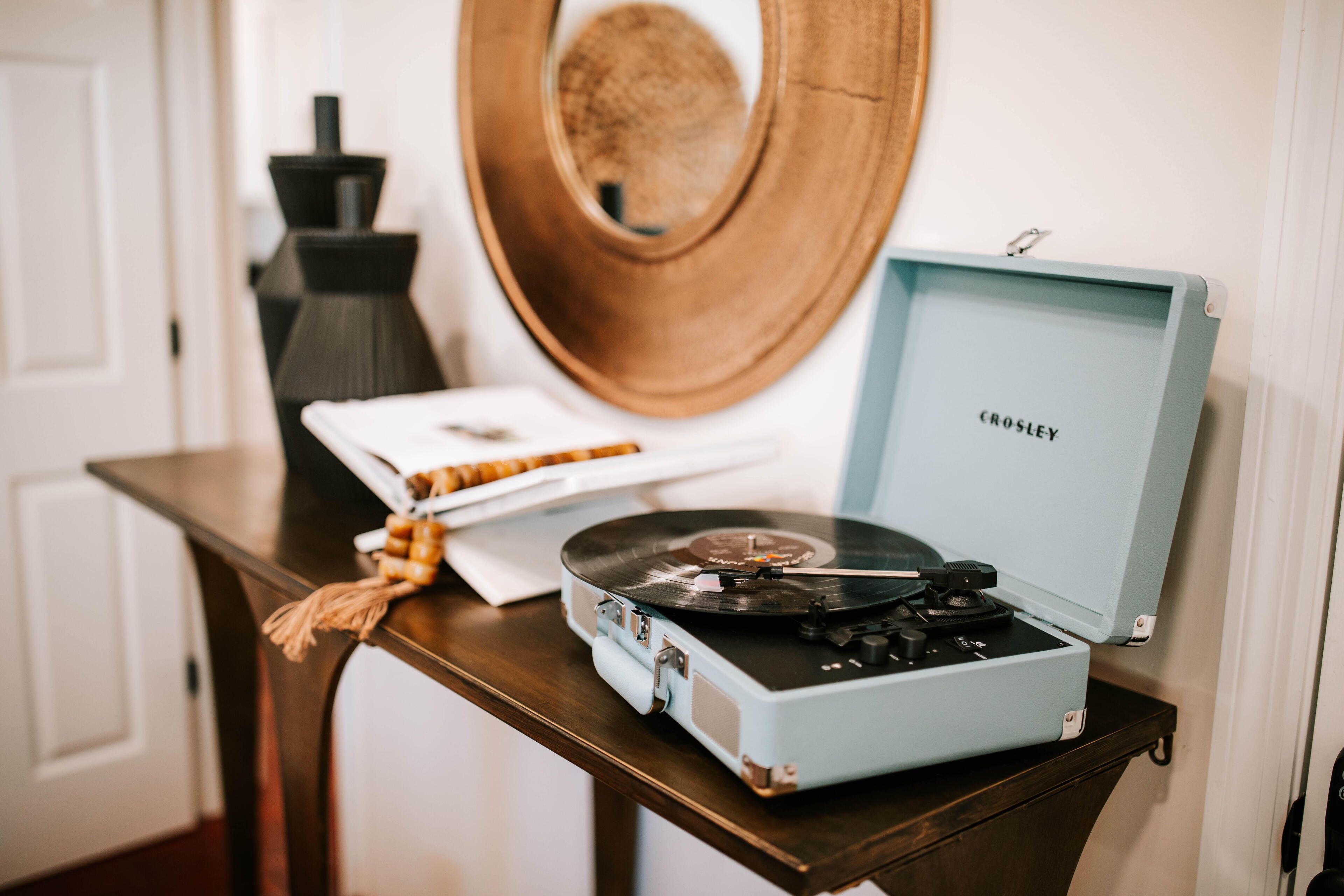 Tocadiscos Crosley antiguo sobre una mesa de madera con un plato blanco y un adorno.