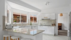 Une cuisine moderne avec des meubles blancs, un plan de travail en marbre et un îlot central intégré avec des tabourets.