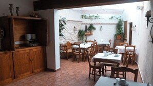 A dining area with wooden tables and chairs, a kitchen area with cabinets and a stove, and a stone wall with plants. - CASA RURAL & SPA LA GRAJA (Chinchón)