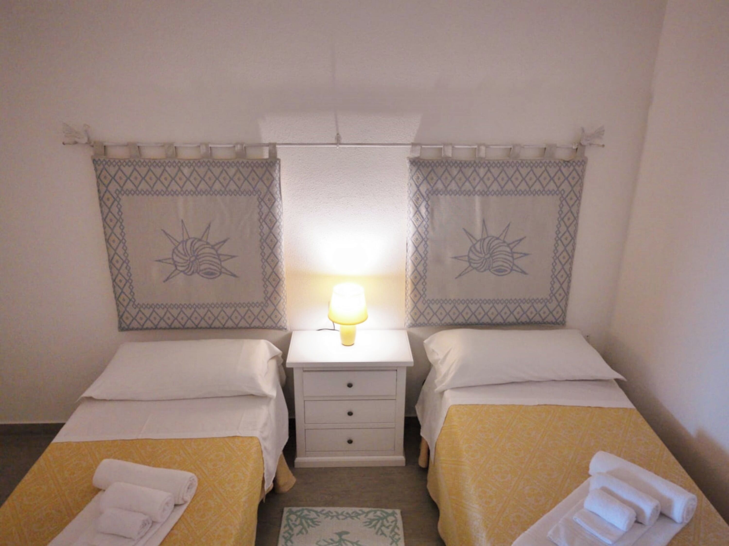 Una habitación de hotel con dos camas individuales, una mesita de noche con lámpara y un cabecero estampado.