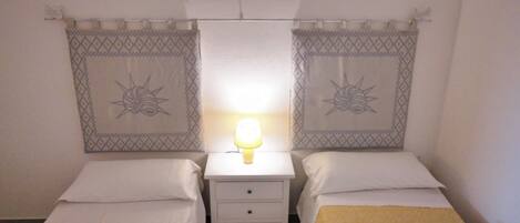 Una habitación de hotel con dos camas individuales, una mesita de noche con lámpara y un cabecero estampado.