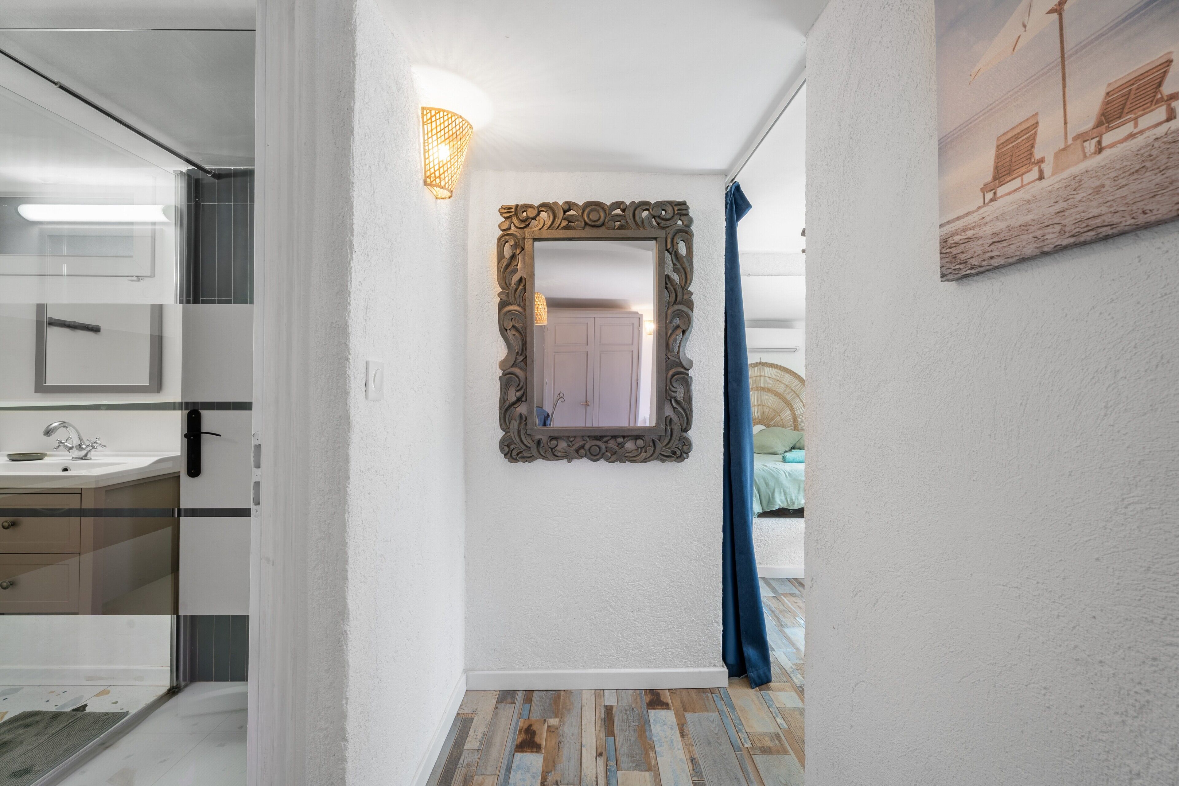 A hallway with a mirror, a light fixture, a door, and a painting on the wall.