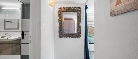 A hallway with a mirror, a light fixture, a door, and a painting on the wall.