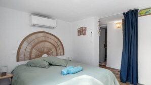 A bedroom with a bed, a wall-mounted air conditioner, a wicker headboard, and a blue curtain. - Charming Provençal Cottage, 900 m from the Beach (Sanary-sur-Mer)