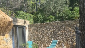 A stone-walled outdoor area with a blue lounge chair, a small table, and a thatched roof structure. - Charming Provençal Cottage, 900 m from the Beach (Sanary-sur-Mer)