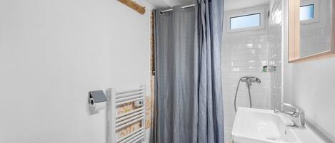 A bathroom with a toilet, a shower with a curtain, a sink, and a mirror.