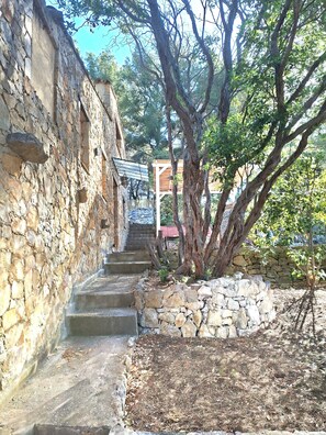 A stone staircase leading up to a wooden structure, surrounded by trees and a stone wall.