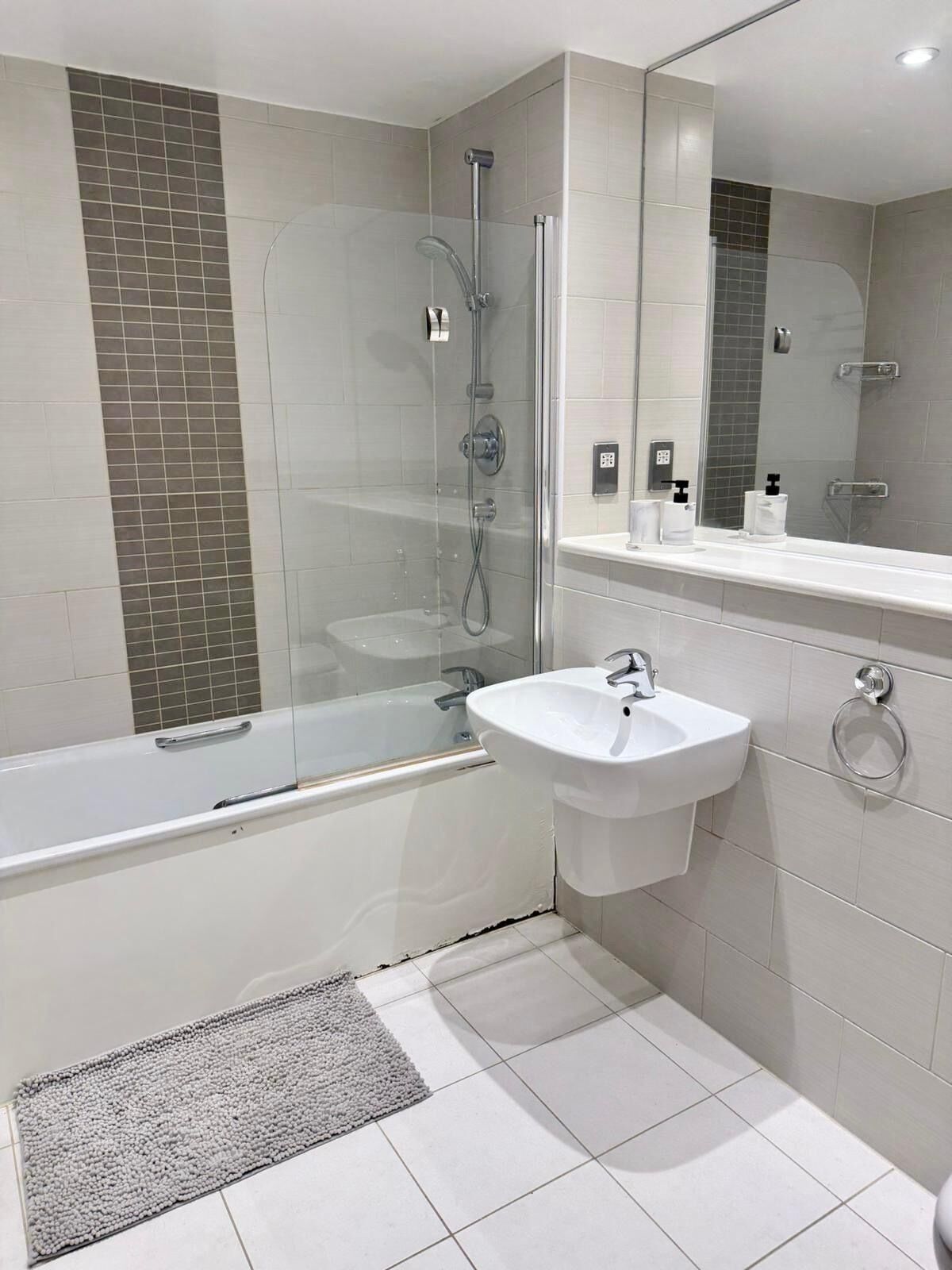 A modern bathroom with a glass-enclosed shower, a white bathtub, and a sink with a towel ring.