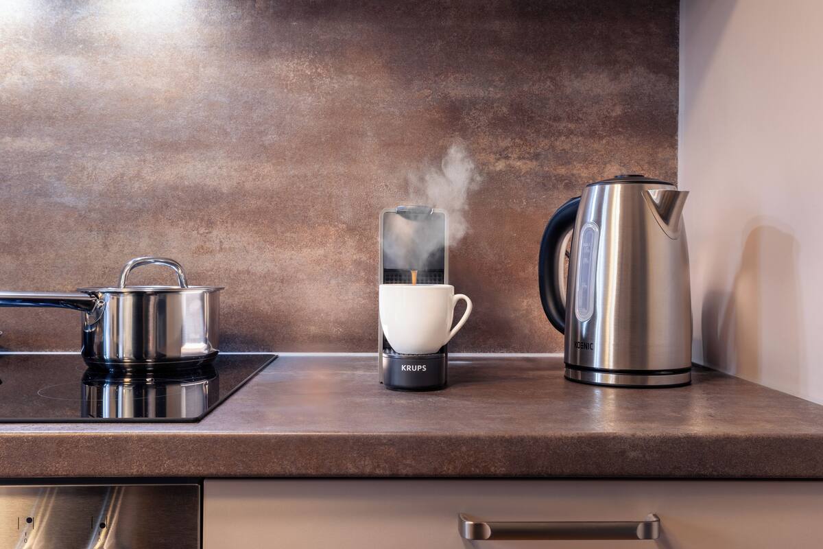 Een aanrecht met een waterkoker, een koffiezetapparaat en een pan op een inductiekookplaat.