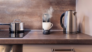 Un plan de travail de cuisine avec une bouilloire, une machine à café et une casserole sur une plaque de cuisson à induction.
