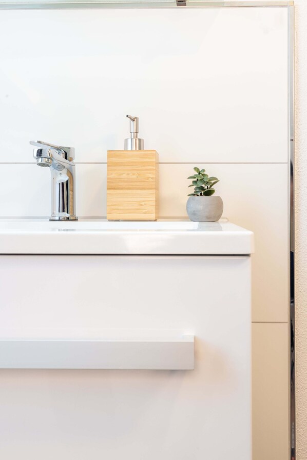 A bathroom with a white sink, a modern faucet, a wooden block, and a small potted plant. - Weisser Ochsen - smart living by corents (Schwaebisch Gmuend)