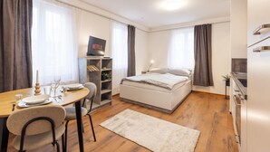 Une chambre moderne comprenant un lit, un bureau avec une chaise, un téléviseur et un coin cuisine.