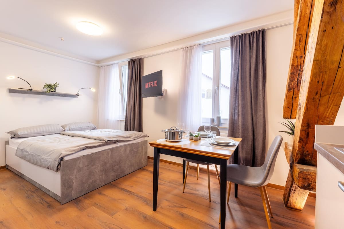 Een moderne kamer met een bed, een eettafel met stoelen, een aan de muur bevestigde televisie en een houten accentmuur.