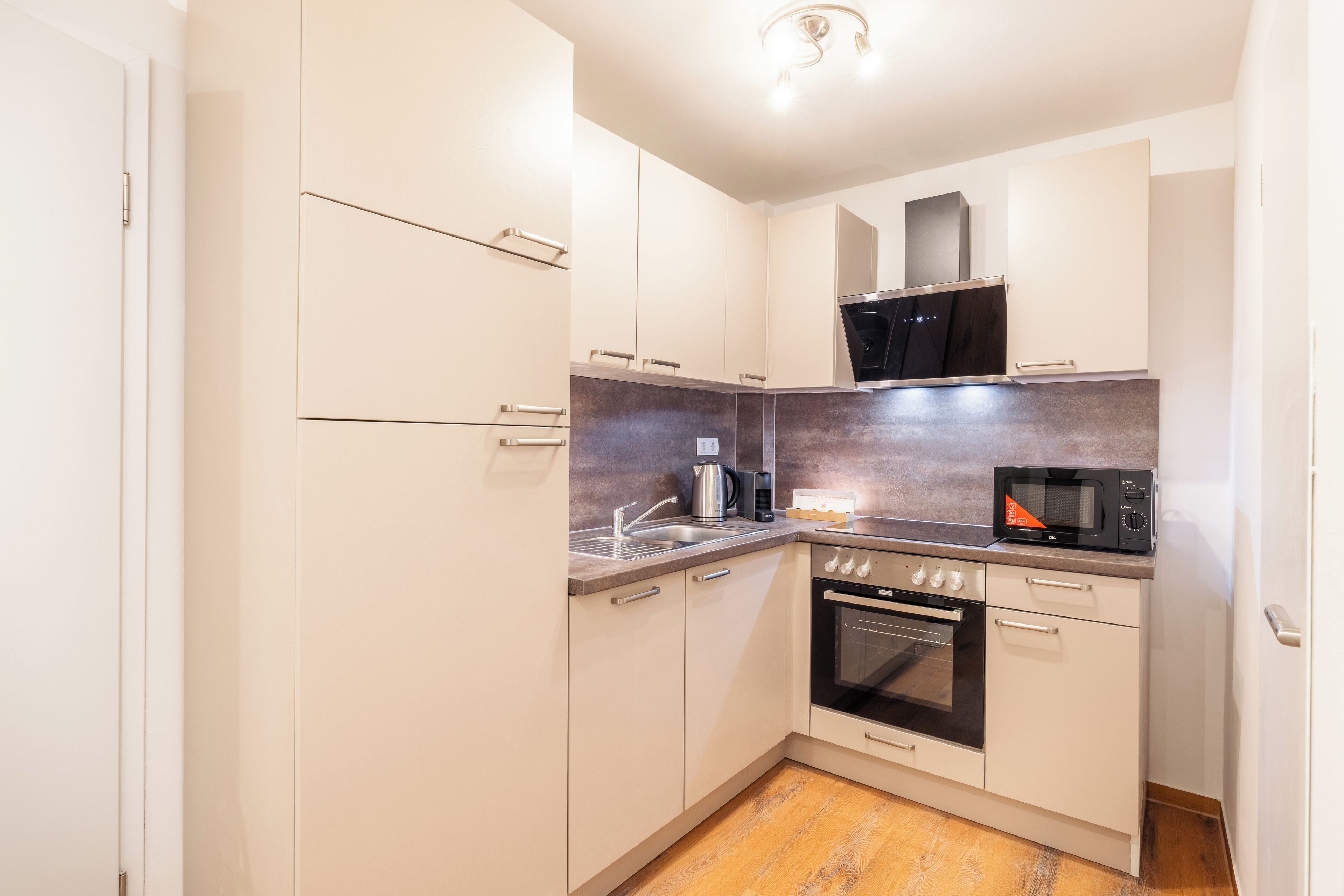 A compact kitchen with white cabinets, a stainless steel range hood, a microwave, and an oven.