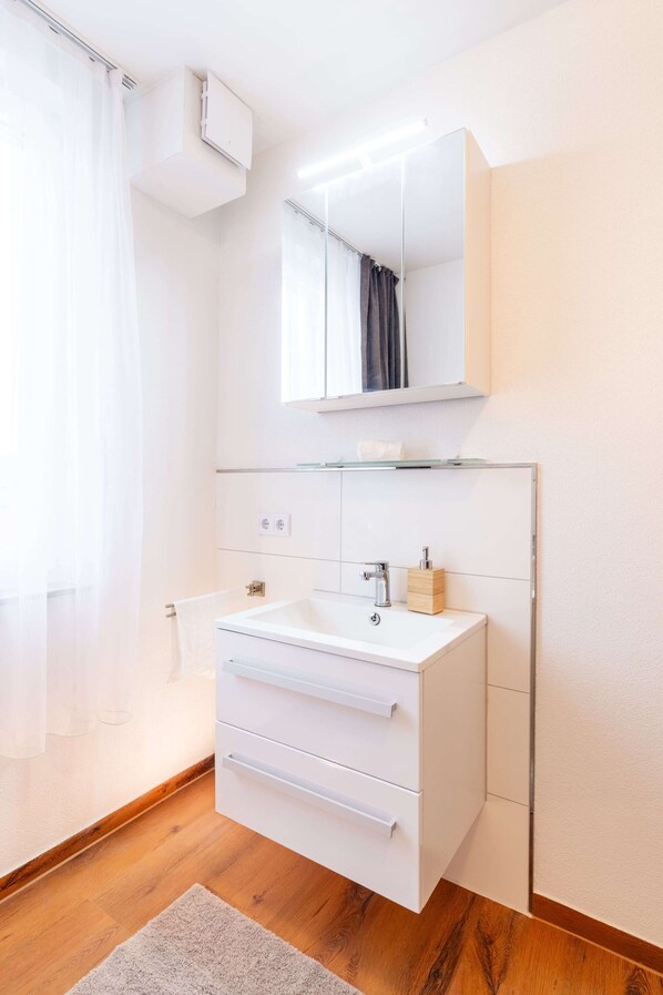 Un baño moderno con tocador blanco, cabina de ducha con mampara de vidrio y un espejo grande.