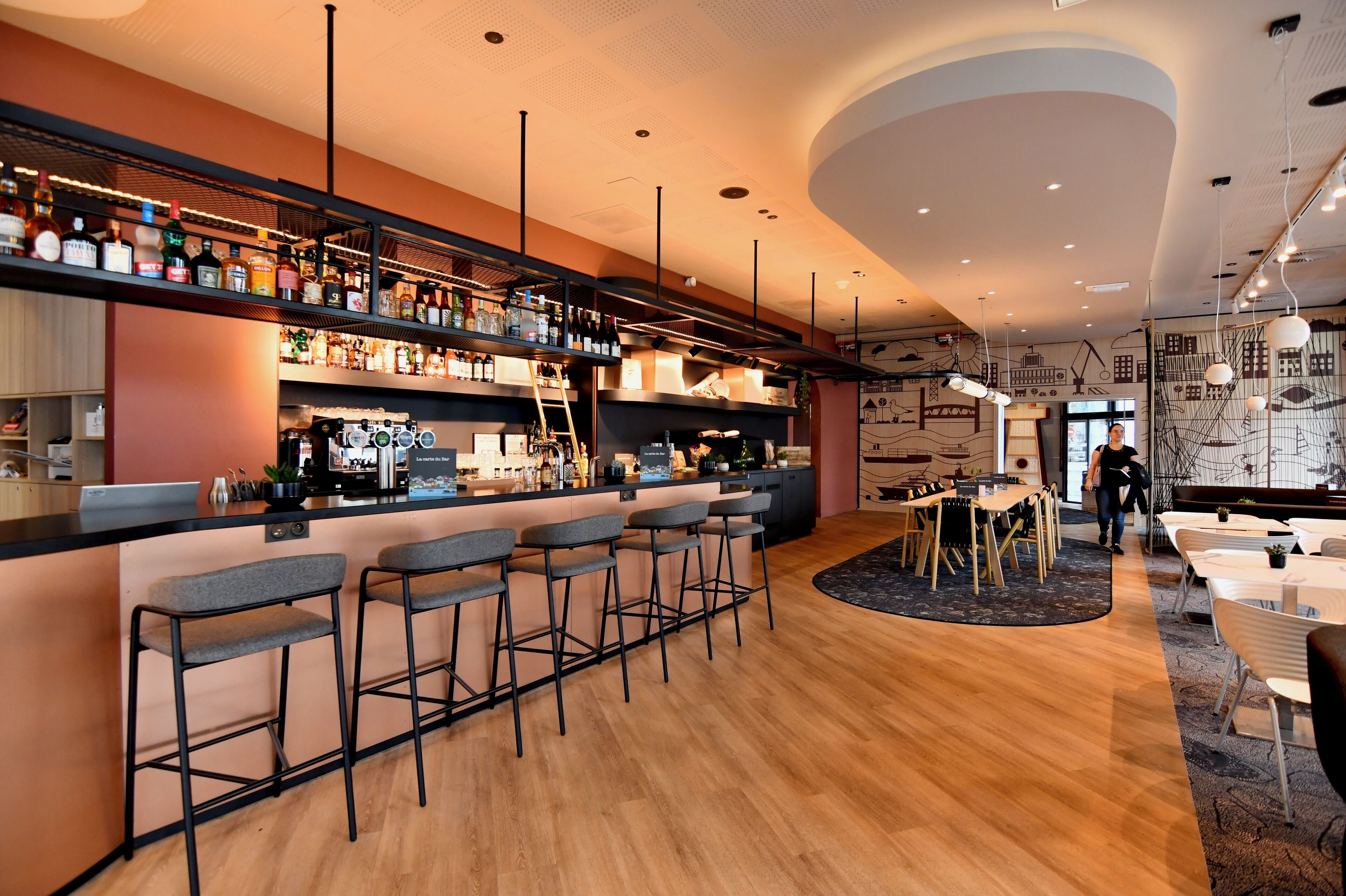 A modern bar area with a long counter, multiple stools, and a variety of bottles.