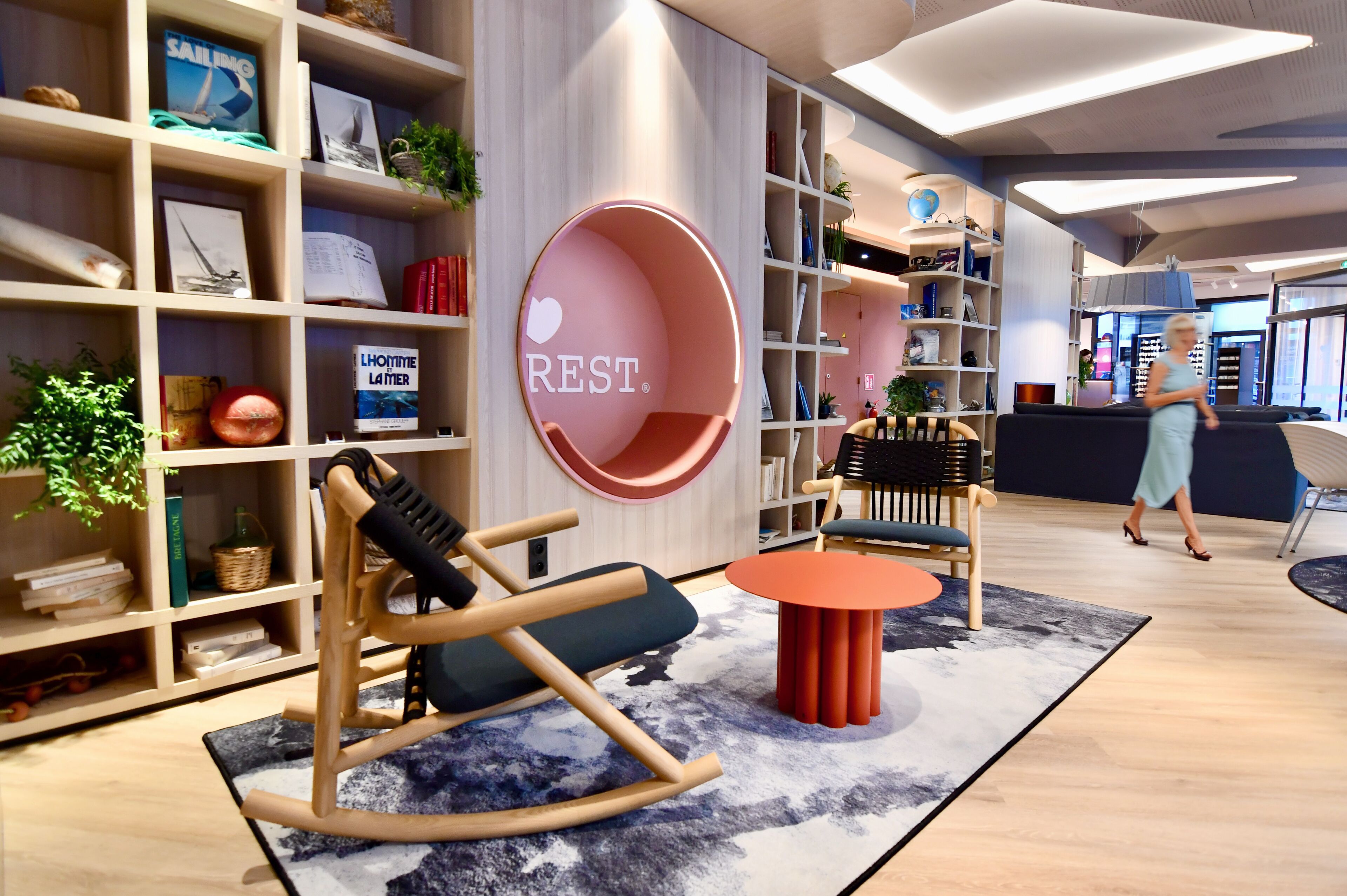 A modern interior with a rocking chair, a circular seating area, and a bookshelf filled with books and decorative items.
