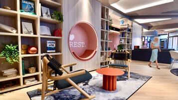 Un interior moderno con una mecedora, una zona de estar circular y una estantería llena de libros y objetos decorativos.