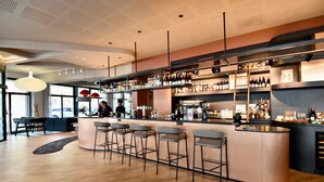 A modern bar area with a curved counter, multiple stools, and a variety of bottles and glasses on shelves. - ibis Budget Brest Centre Port (Brest)